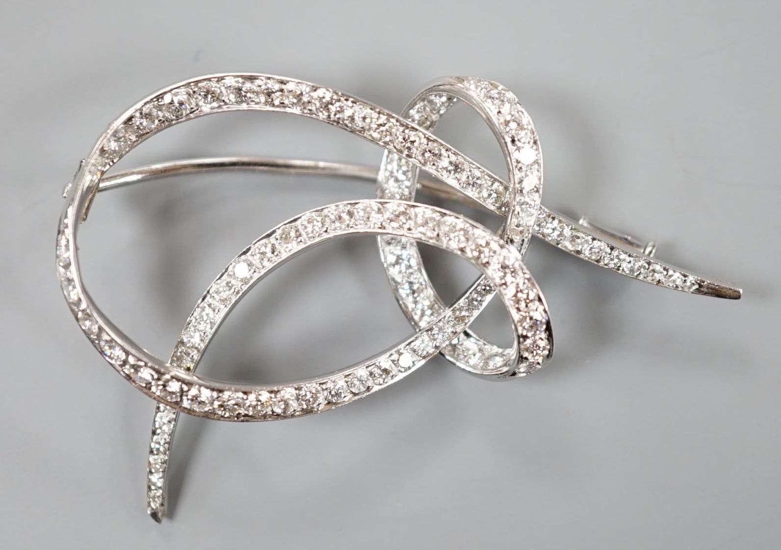 A white metal and diamond cluster set scroll brooch, 52mm, gross weight 14 grams.